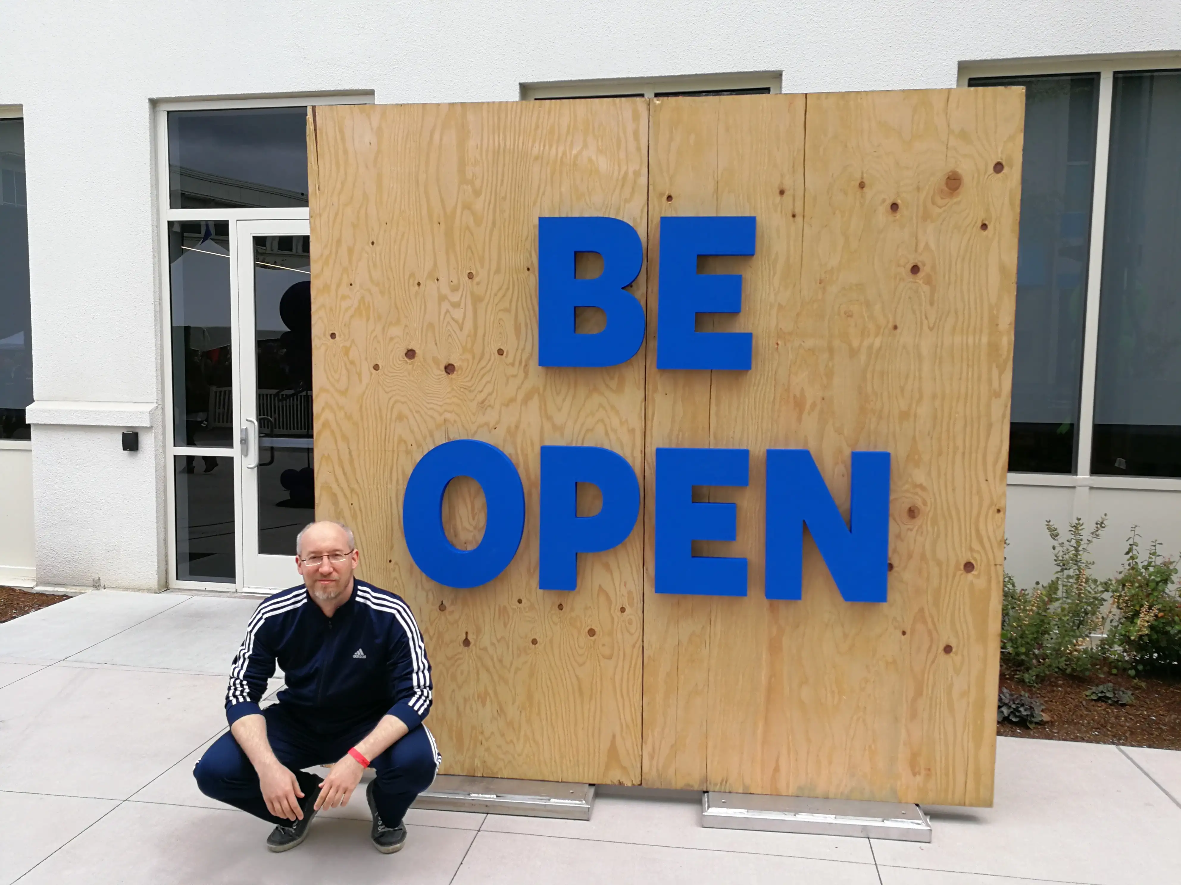 Dmitry Borodaenko squatting in front of a 'Be Open' sign on Facebook campus